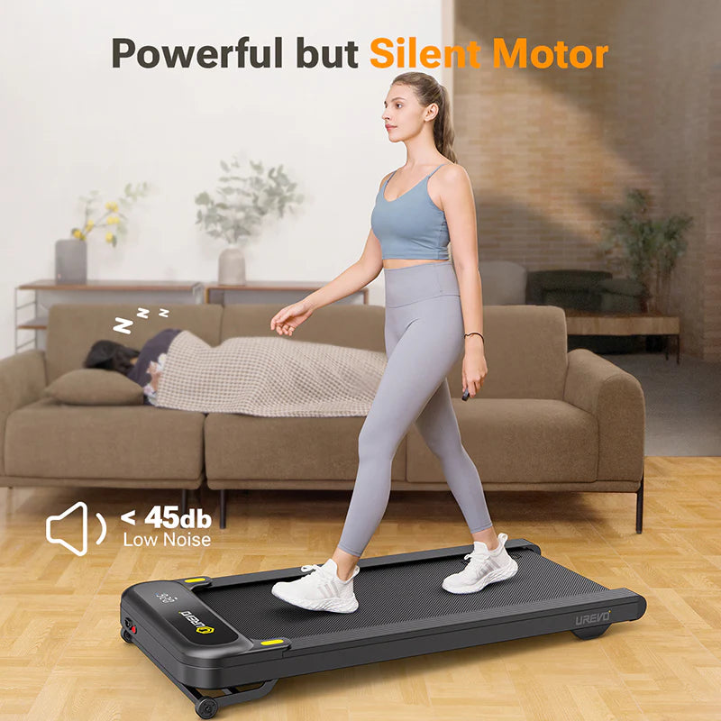 A woman walking on a treadmill in a living room, with a person sleeping on the couch behind her.