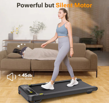 A woman walking on a treadmill in a living room, with a person sleeping on the couch behind her.