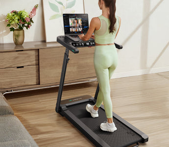  A woman in light green workout clothes is using a treadmill with a laptop.