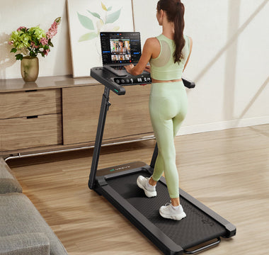 A woman uses a treadmill with a laptop, exercising while working.