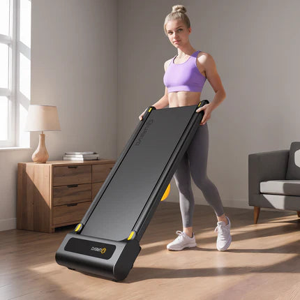 A woman in workout attire is holding a compact treadmill in a living room.