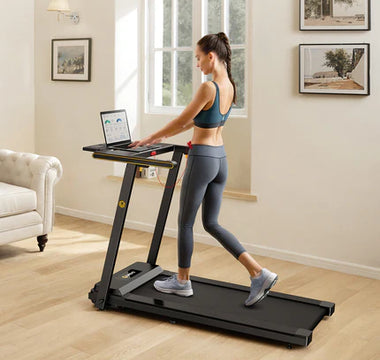 Woman walking on a treadmill while using a laptop in a home setting.